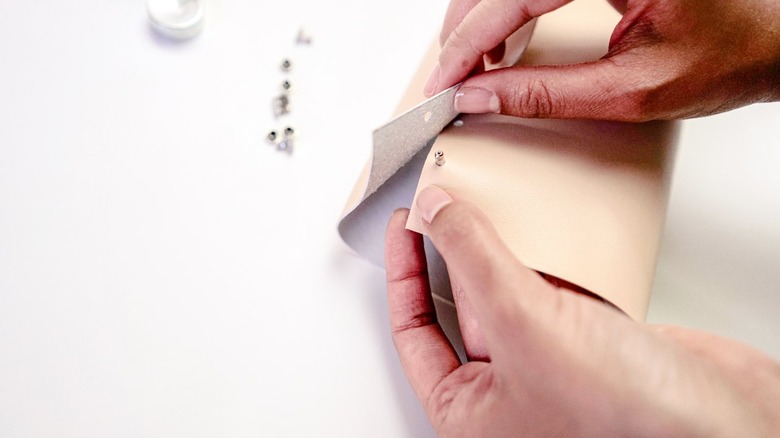 Hands assembling beige leather vase with silver rivets