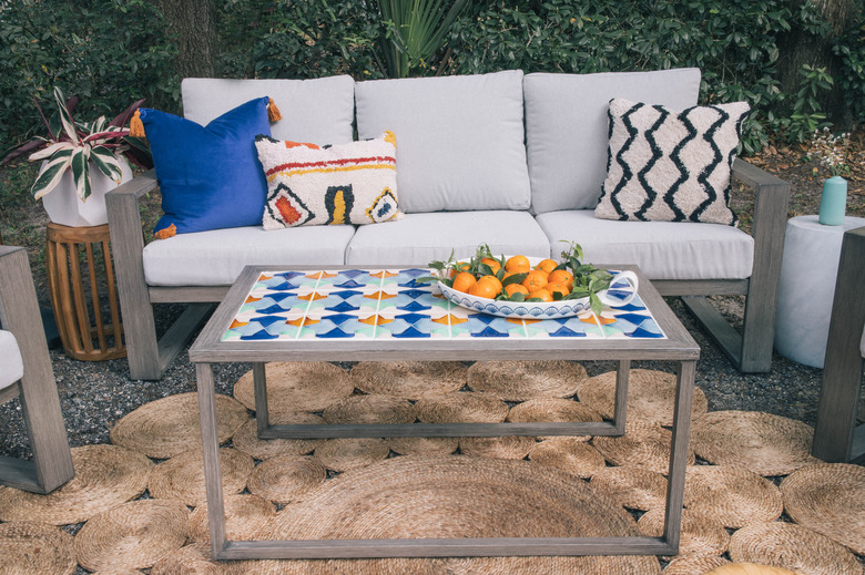 DIY tiled coffee table in outdoor patio with a bowl of oranges on top in front of sofa with colorful pillows