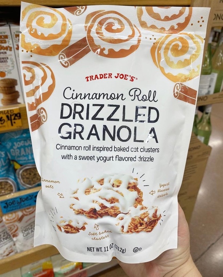 A white bag of Trader Joe's cinnamon roll drizzled granola. There are drawings on cinnamon rolls and cinnamon sticks at the top