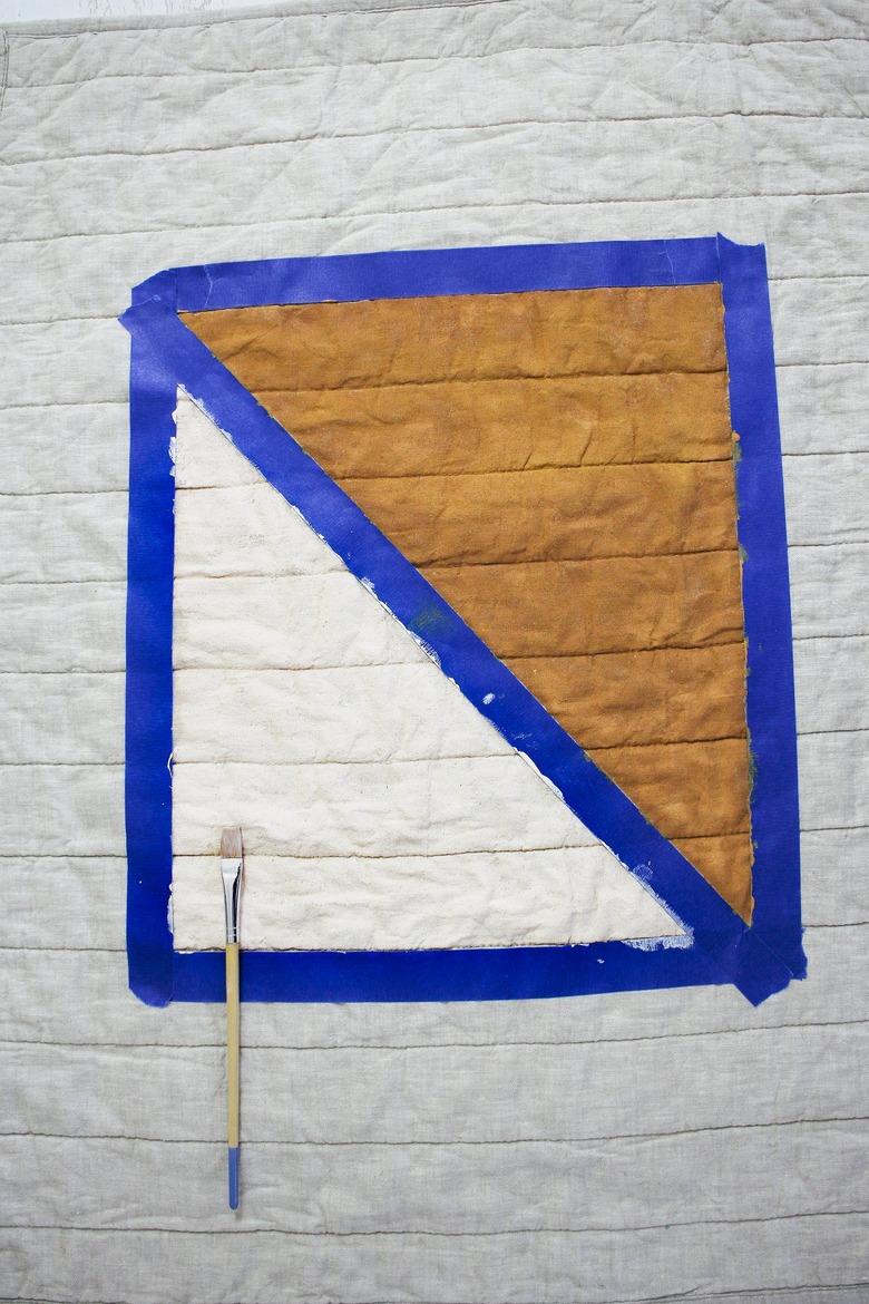 Quilted pillow with blue painter's tape blocking brown and white design with paintbrush