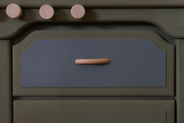 Drawer front of nightstand painted gray to create an oven with a wood handle attached in the center