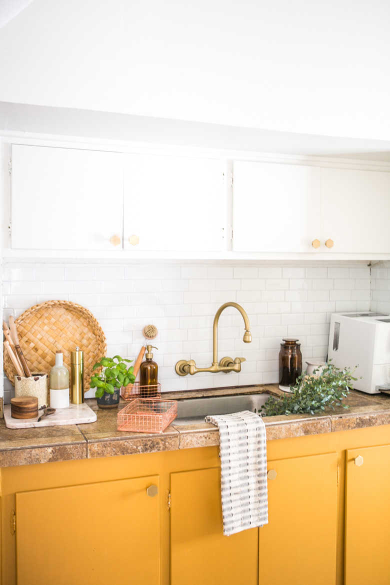 kitchen space with white and mustard cabinets and gold sink faucet