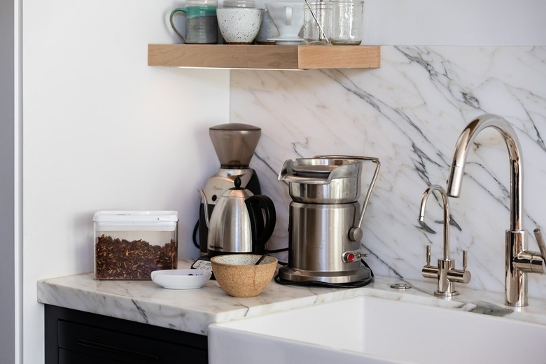 Granite backsplash and countertop with sink under wood shelf with glassware