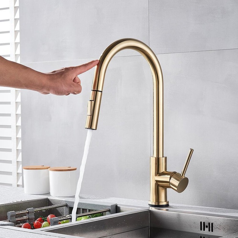 A person touching the brass kitchen faucet to turn it on