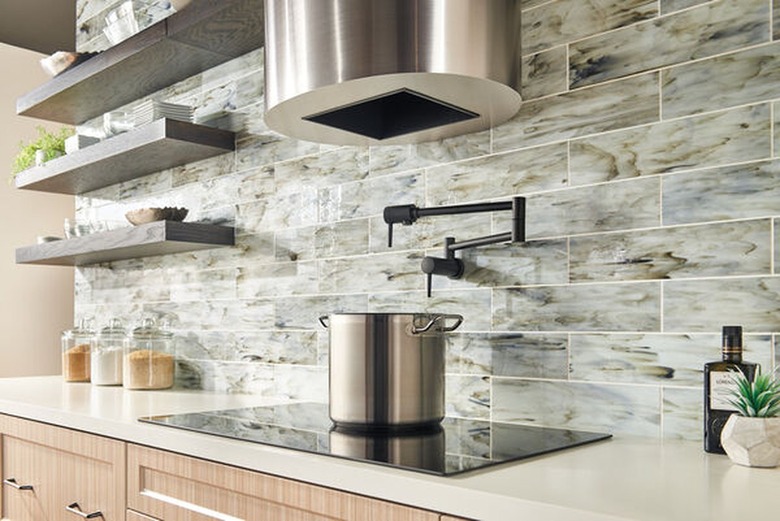 A black chrome pot-filler faucet in a kitchen with gray subway tiles and open shelving