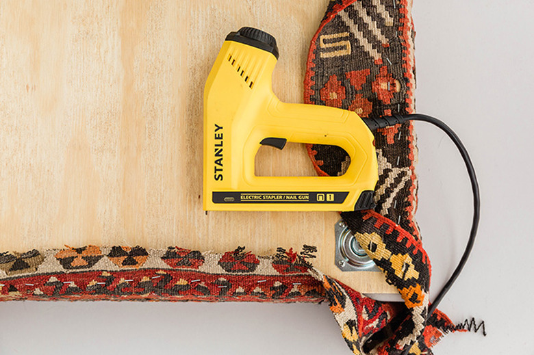 Staple the rug around the sides of the plywood board.