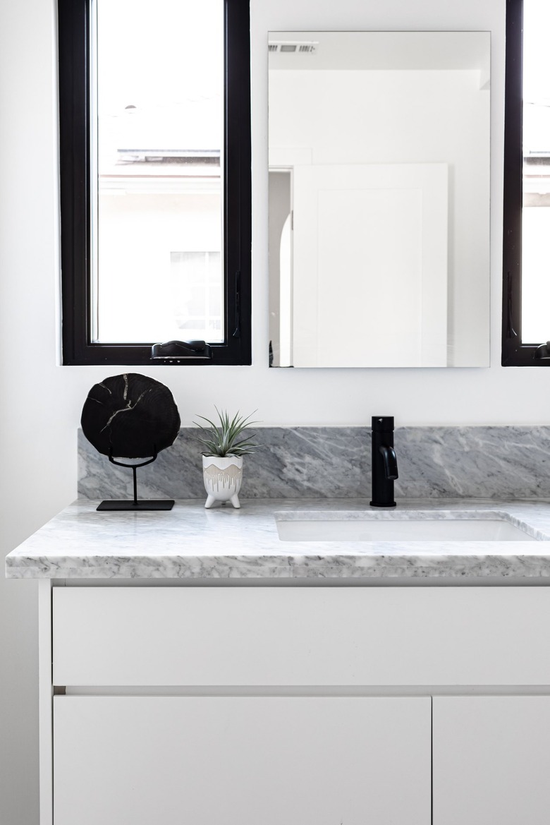 White cabinets and marble countertop for sink in bathroom with mirror and small plant