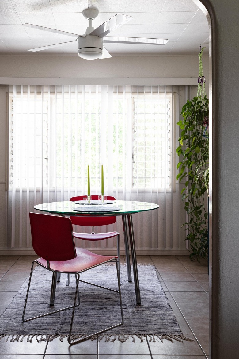 Two red chairs at a round dining table with two candle holders. Sheer curtains
