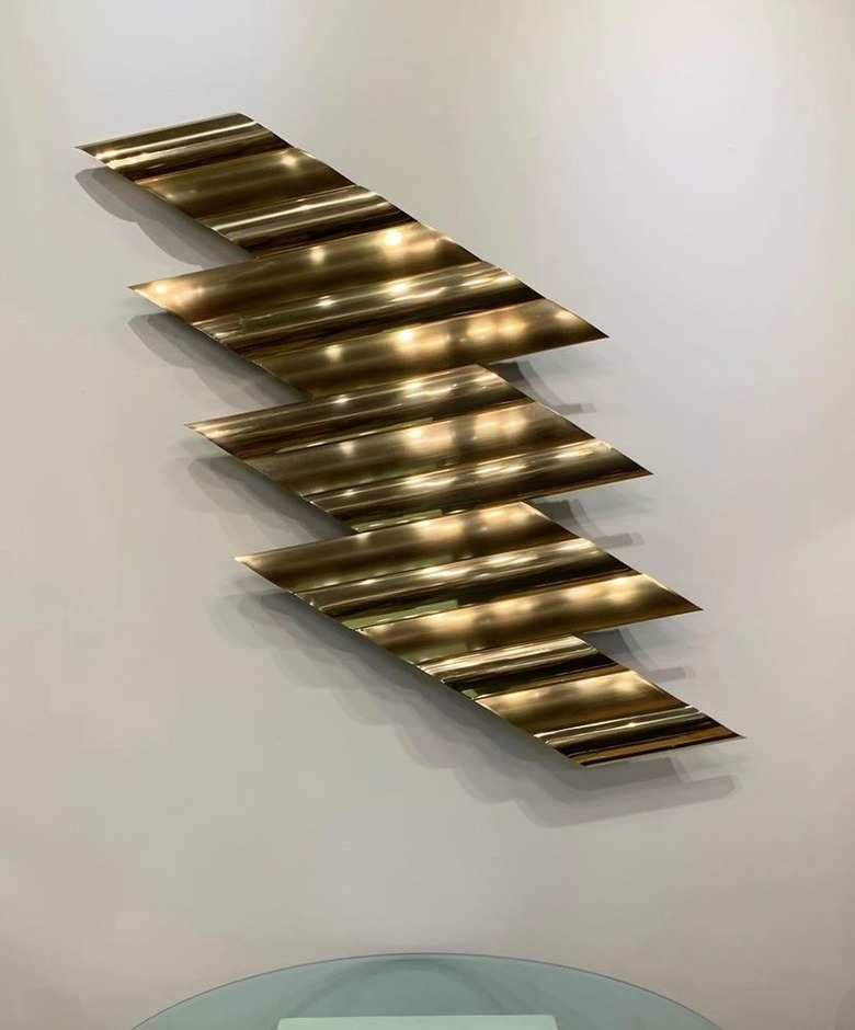 A brass lighting bolt wall sculpture on a white wall.