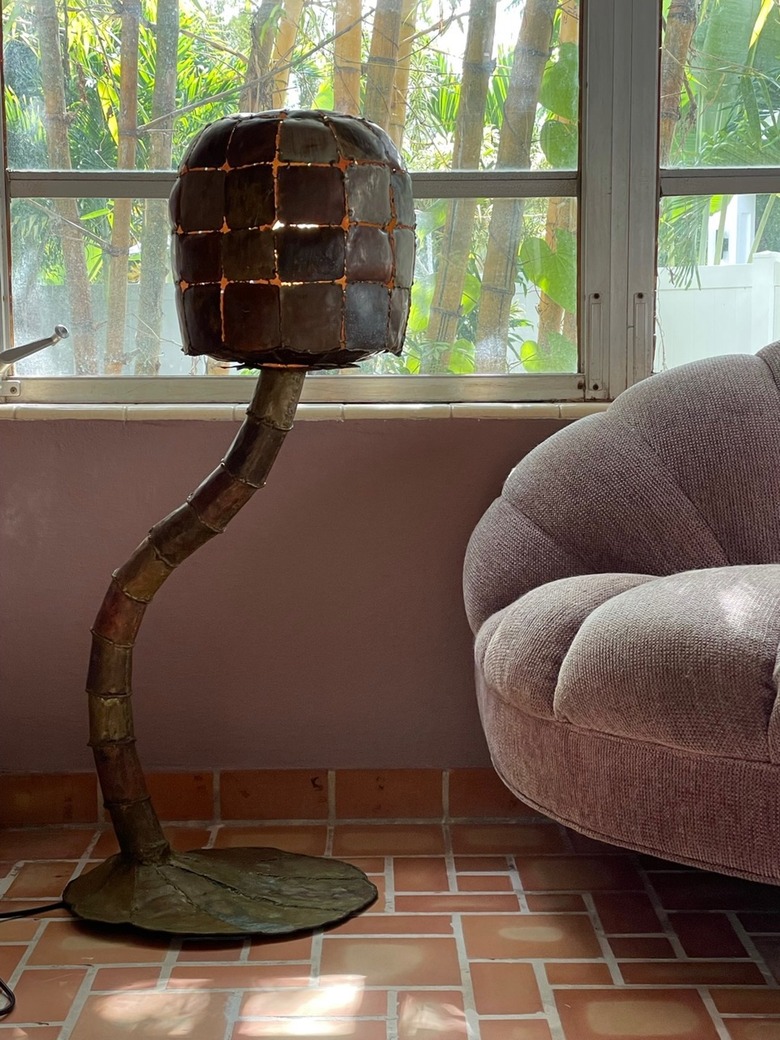 A dark patchwork metal floor lamp in a light-filled room with terra cotta-colored floor tile.