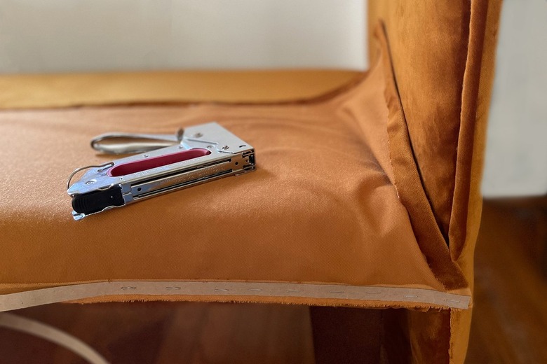 Stapling fabric skirt to bench with staple gun and cardboard tack strip