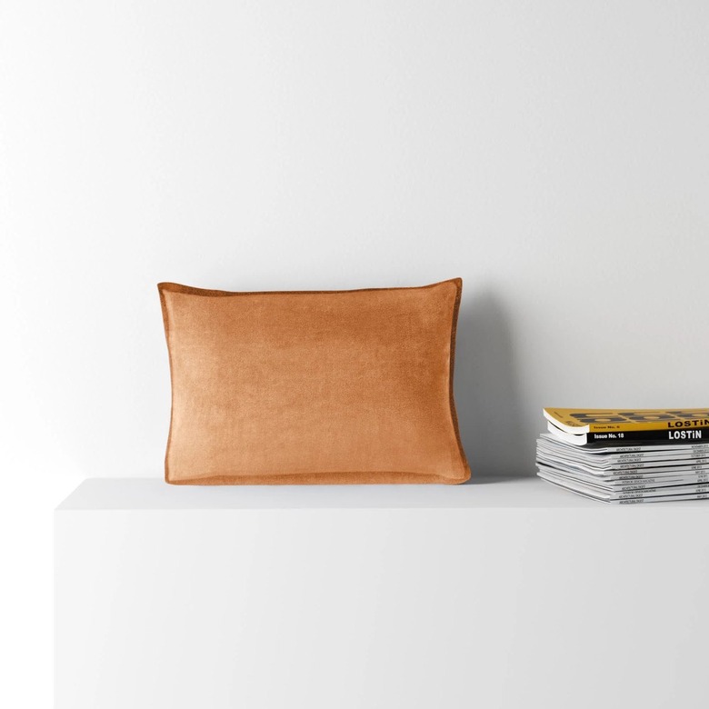 burnt orange velvet pillow next to stack of magazines