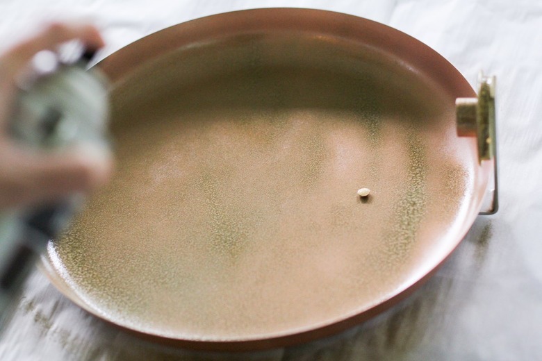 Gold spray paint being applied to round metal plate