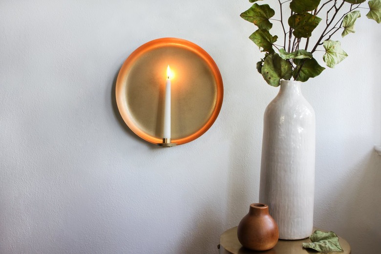 Round sconce with candle next to white vase with plant