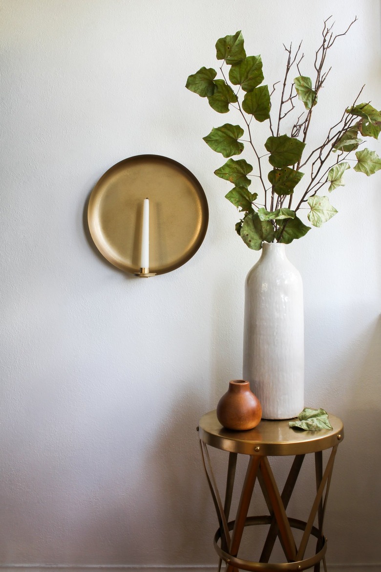 Wall sconce with candle next to small table with vase with plant