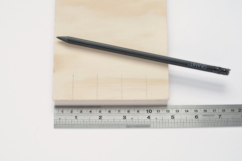 a ruler and a pencil next to a square of plywood that has pencil marks at regular intervals