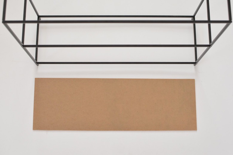 Carboard panel laying next to black metal shelving frame against a white background