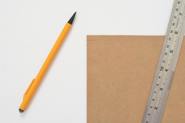 Metal ruler laying flat on top of cardboard panel next to mechanical pencil against a white background