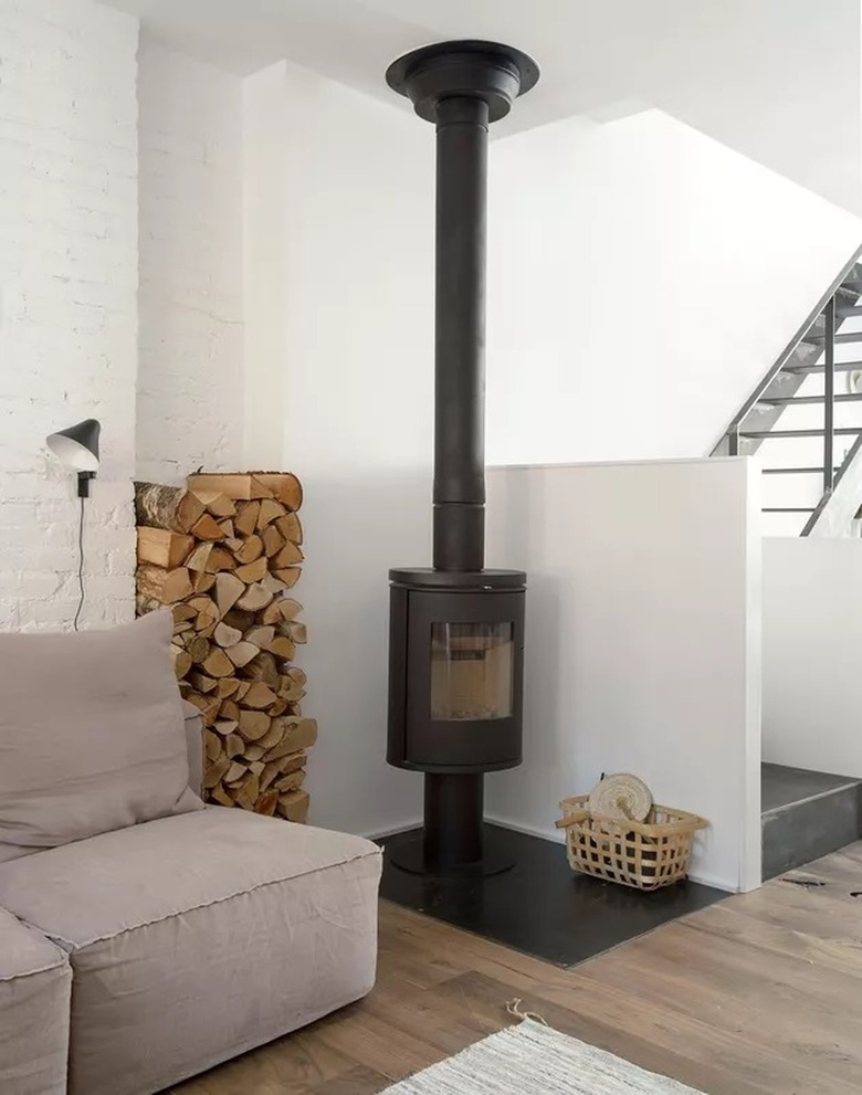 White living room with a small stove and wood pile in the corner