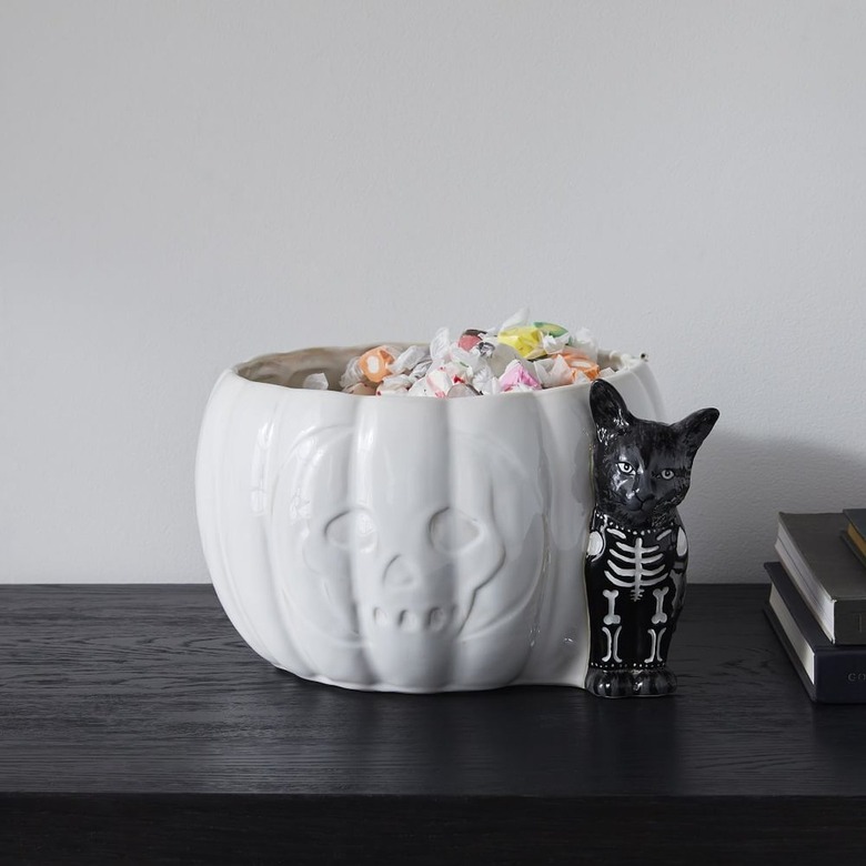 White Halloween candy bowl shaped like a pumpkin with a black cat full of candy.
