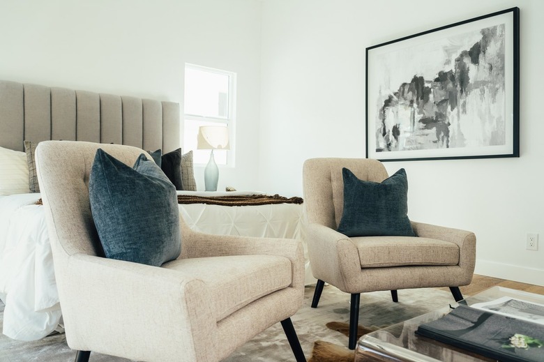 bedroom with gray headboard and beige accent chairs