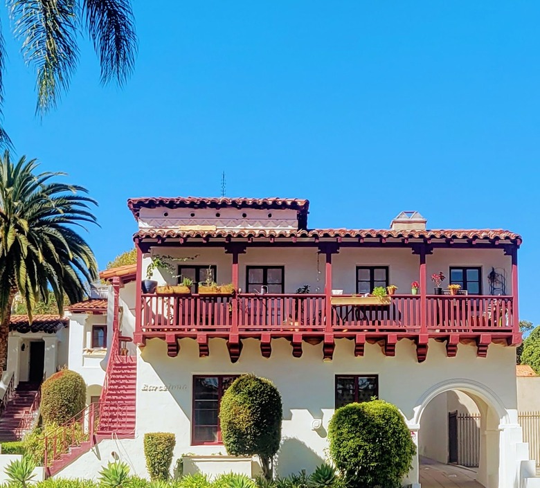 White Mission style apartment building with burgundy balcony and red tile roof