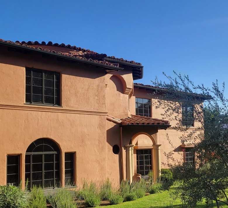 Two-story Spanish-style home painted rust with red-tile roof and green garden
