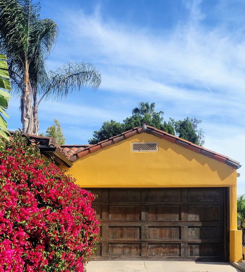 Mustard garage with dark wood garage door and red tile roof by bougainvillea busth