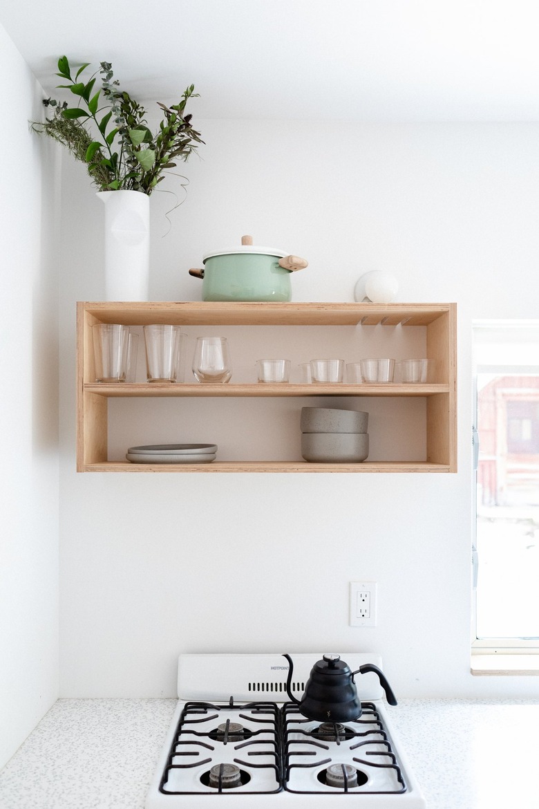 A minimalist white walled kitchen and wood shelving with dishware and plant