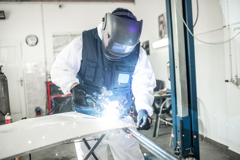 Car body shop technician using a MIG welder to repair a damaged car part in a car body shop