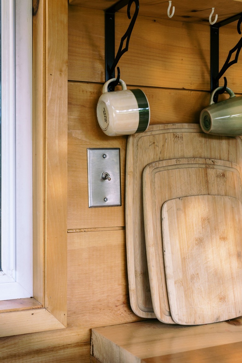 Various cutting boards and hanging cups against wood-paneled wall