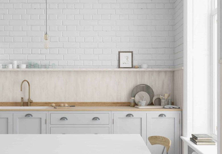 Light gray kitchen cabinets with wood backsplash and brick wall