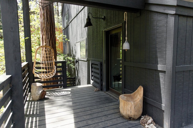 A wood deck of a black cabin. A hanging boho chair