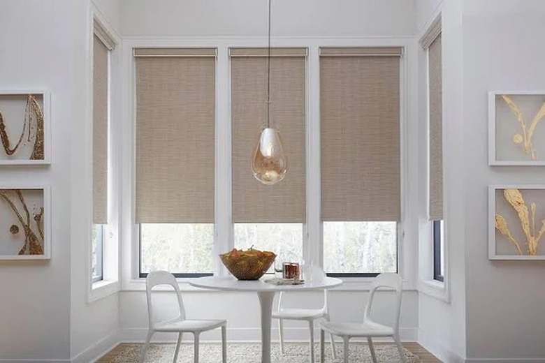 A dining room with neutral colored roller shades on the windows