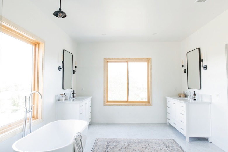 A bathroom with a light wood frame window. Double white vanities
