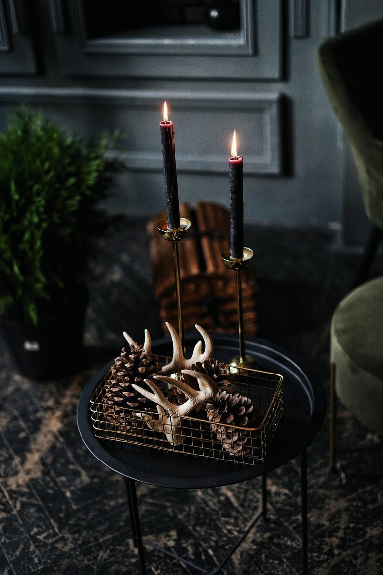 Antlers and pinecones sit in a metal basket atop a dark side table