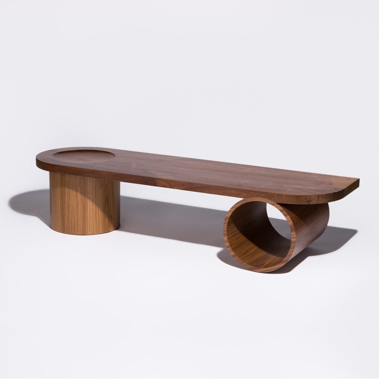 A long dark wood bench with one leg being thick and chunky