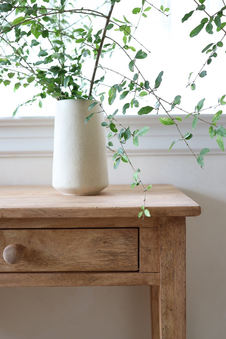 Distressed wood table with vase of tall green leaves on top