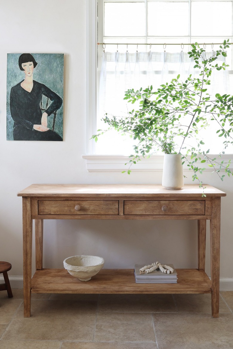 Distressed wood table in kitchen with an oil painting and vase of tall green leaves