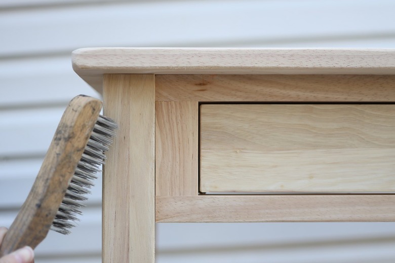 Scuffing up the surface of a wood table with a wire brush
