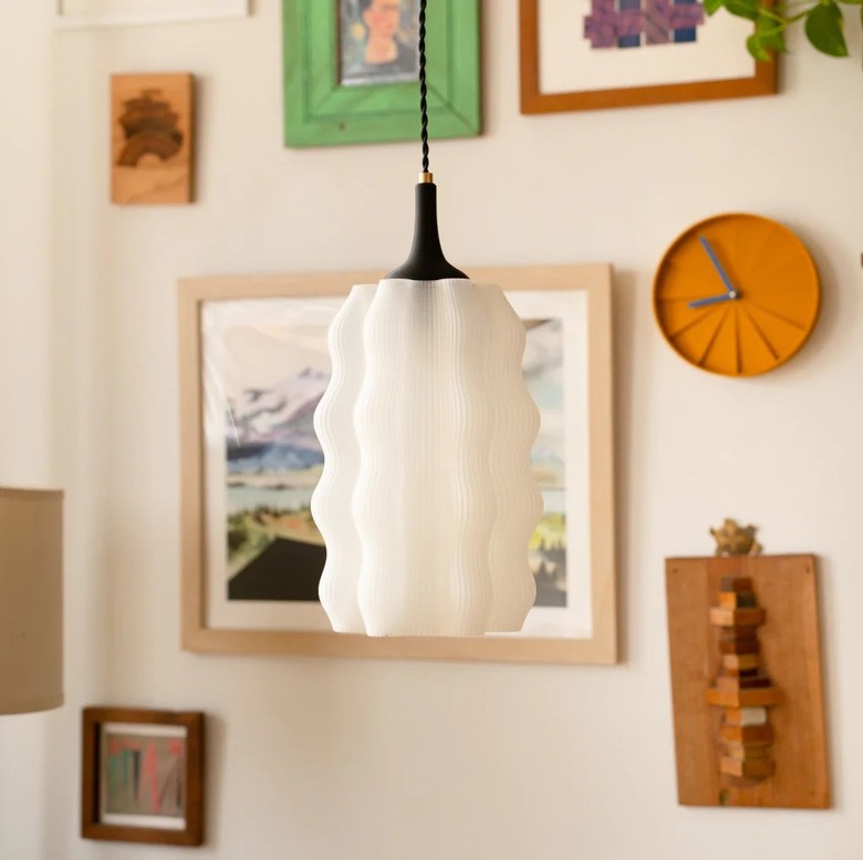 A wavy pendant lamp shade attached to the ceiling with a black wire. Behind the lampshade