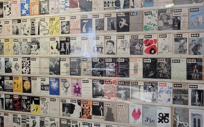 Numerous covers of ONE Magazine are arranged in a gridlike fashion behind glass