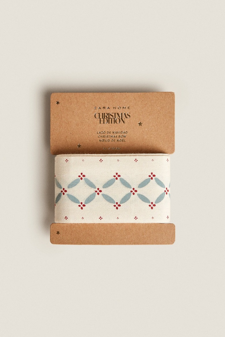 A cardboard spool of ribbon with a red and green holly pattern down the center of it.