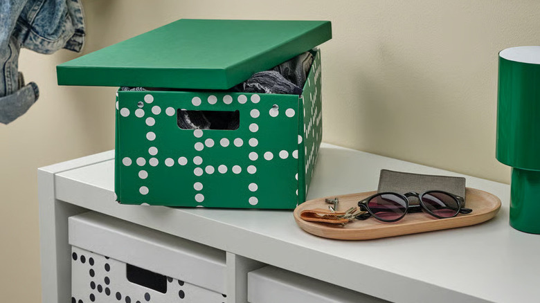 A bright green lidded box sits next to a wooden accessory tray on a white shelf