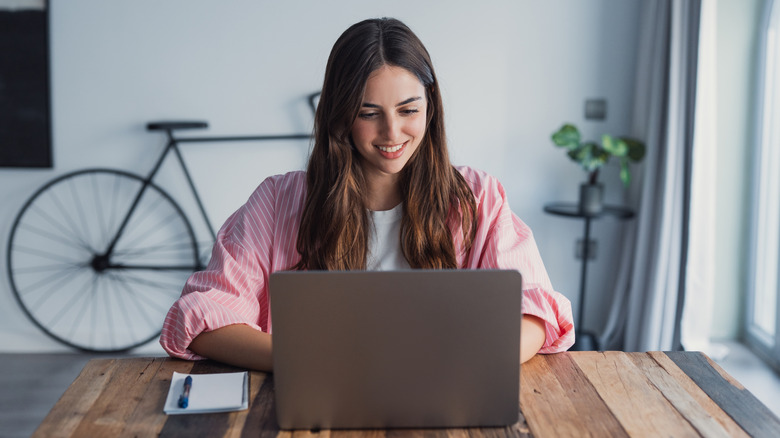 A young woman smiles while working on a laptop