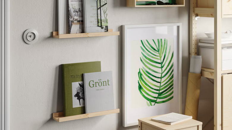 Books are displayed on two thin pine shelves next to a large botanical print
