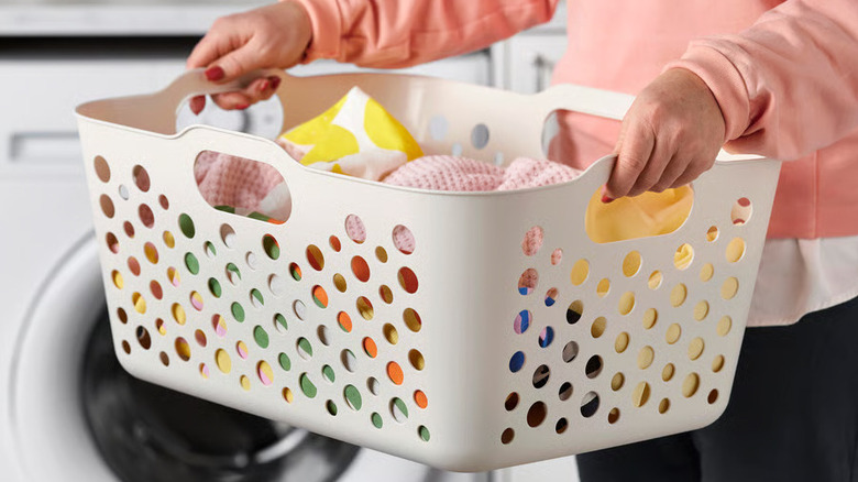 A person holds a small SLIBB Laundry basket full of brightly colored clothes