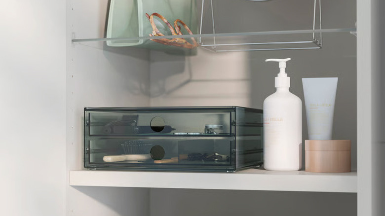 Toiletries surround a dark gray VISSLAÅN Mini chest in a bathroom closet