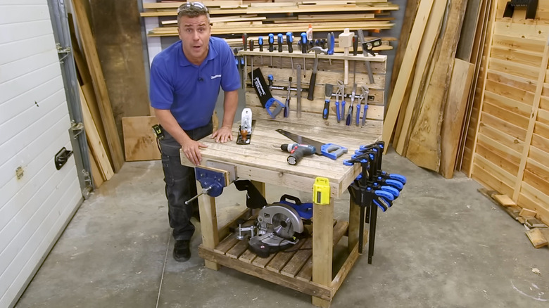 A man standing beside a basic pallet wood workbench with tools
