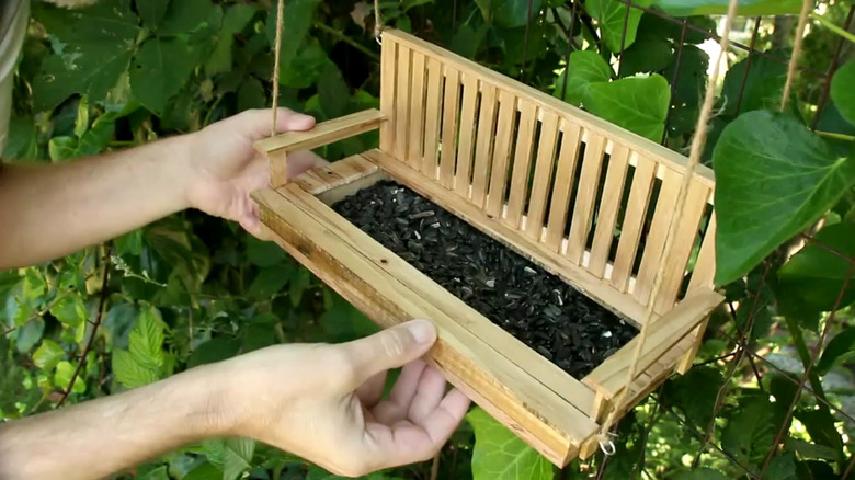 hand showing off his pallet wood bird feeder made to look like a porch swing